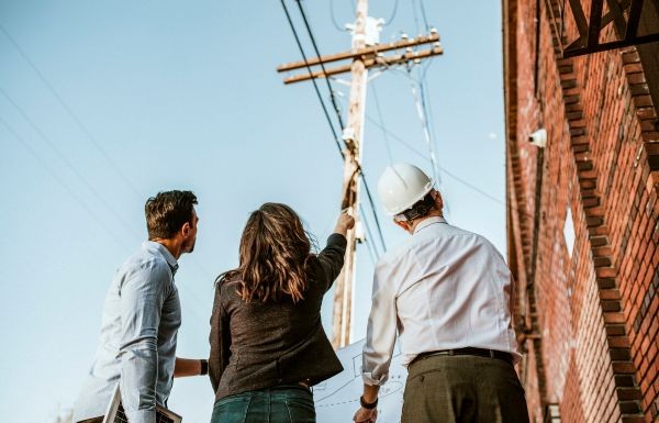 Three people observing overhead power lines near a utility pole.